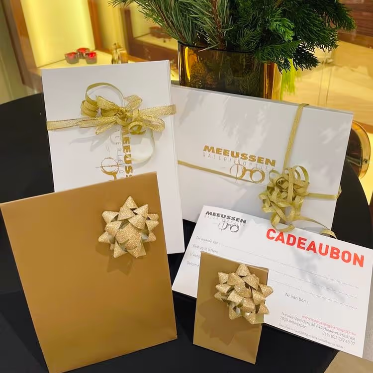 Geschenkbonnen en enveloppen met gouden linten en strikken op een zwarte tafel, naast een vaas met groen takken.