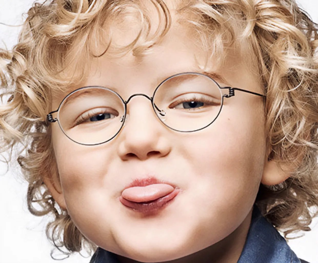 Kind met krullend blond haar en ronde bril steekt de tong speels uit.